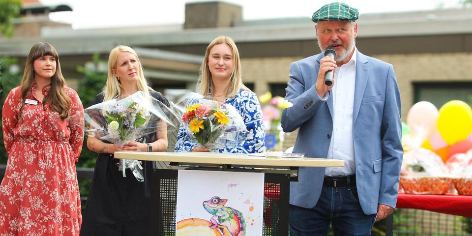 Drei Frauen und ein Mann auf einer Bühne. Der Mann hält ein Mikrophon.