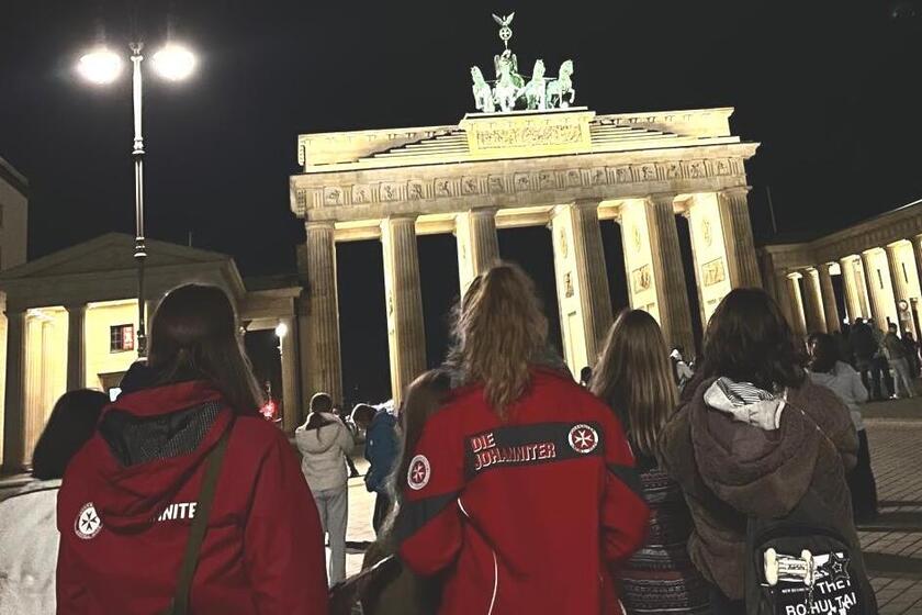 Das Foto zeigt die Reisegruppe der Ferienfreizeit, bestehend aus Kindern und Jugendlichen sowie den Betreuenden der Johanniter-Hochwasserhilfe. Die Gruppe läuft auf das Brandenburger Tor in Berlin zu, das angesichts der abendlichen Dunkelheit hell erleuchtet ist.