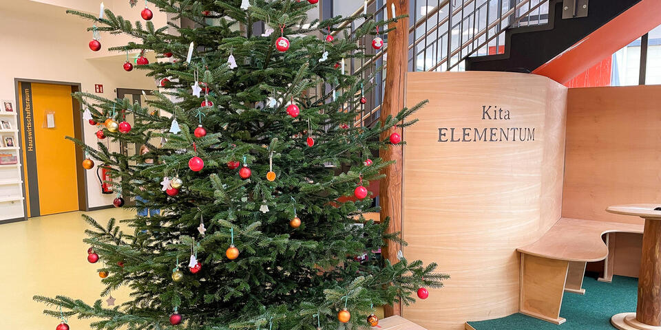 Ein geschmückter Weihnachtsbaum in einem Eingangsbereich. unter dem Baum liegen drei Pakete