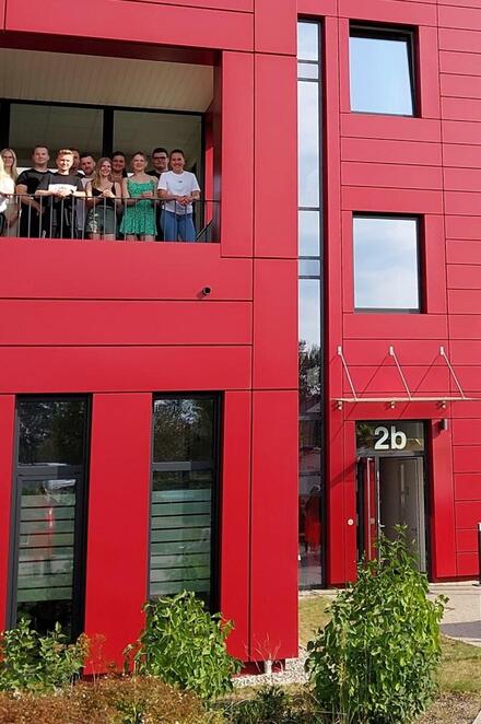 Ein rotes Gebäude mit einem gr0ßen Balkon, auf dem Personen stehen