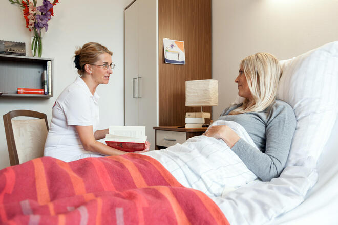 Eine Ehrenamtliche sitzt am Bett einer Frau.