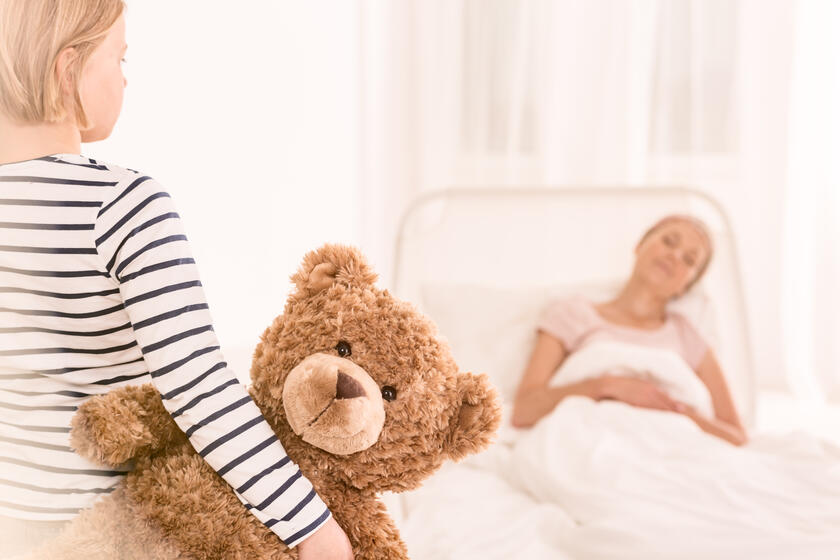 Kleines Mädchen mit Teddy am Bett einer kranken Frau 