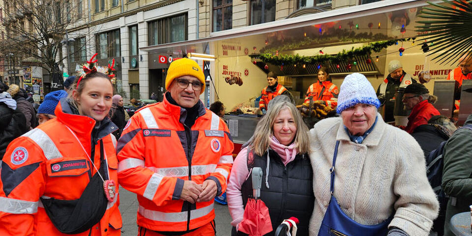 Zwei Johanniter stehen neben zwei Gästen der Johanniter-Suppenküche.
