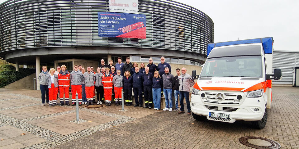 Eine Menschenmenge, teilweise in Einsatzkleidung vor einem runden Gebäude. Neben ihnen ein Rettungswagen