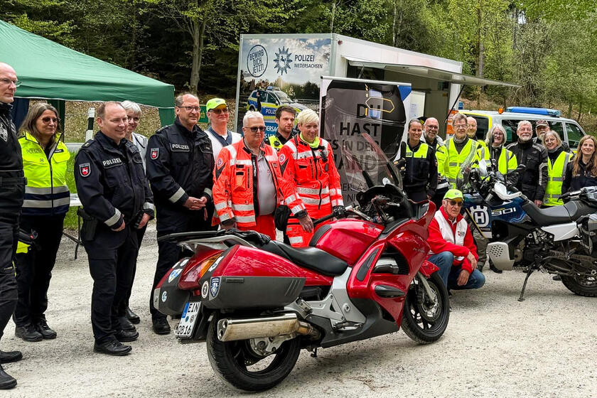 Eine Menschengruppe mit Motorrädern, davon manche in Polizeiuniformen, zwei Johanniter, und andere mit gelben Warnwesten 