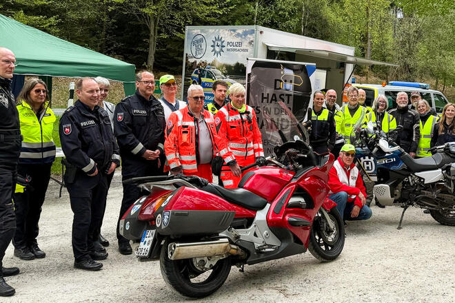 Eine Menschengruppe mit Motorrädern, davon manche in Polizeiuniformen, zwei Johanniter, und andere mit gelben Warnwesten 