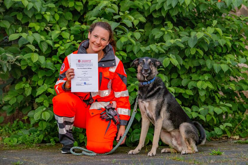 Eine junge Frau kniet neben ihrem Hund und hält ein Zertifikat hoch