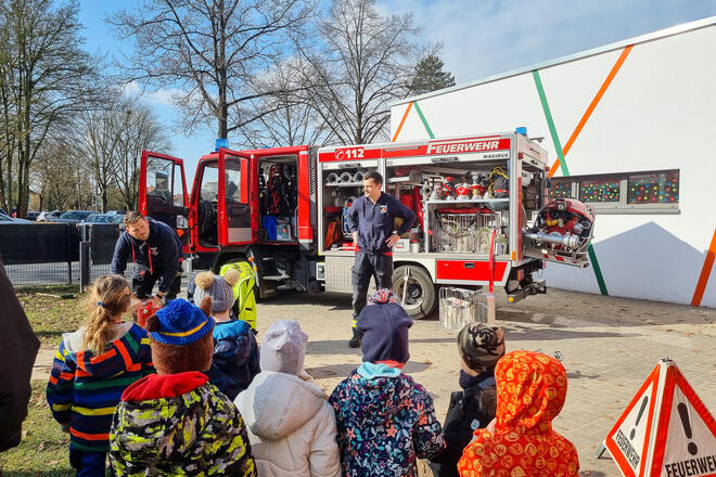 Eine Gruppe von Kindern schauen auf ein Feuerwehrauto. Davor steht ein Mann in Feuerwehrbekleidung