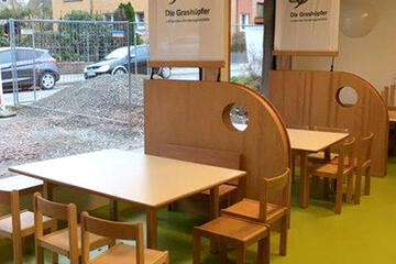 Kleine Stühle und Tische in Holzoptik, auf denen die Kinder und Erzieherinnen und Erzieher bei den Mahlzeiten sitzen können. 