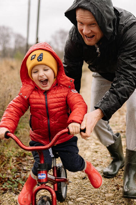Ein Mann schiebt ein Kind auf einem Laufrad.