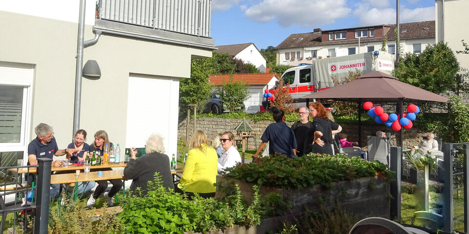 Blick auf Menschen, die auf Bierzeltgarnituren in einem Garten sitzen.