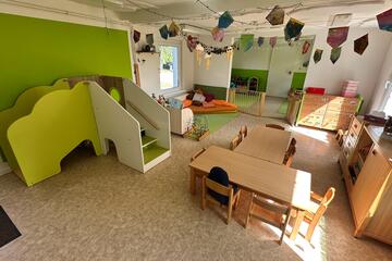 Innenbereich der Kita Landmäuse, grüne Wandfarbe, einer kleinen rutsche, Tischen und Leseecke