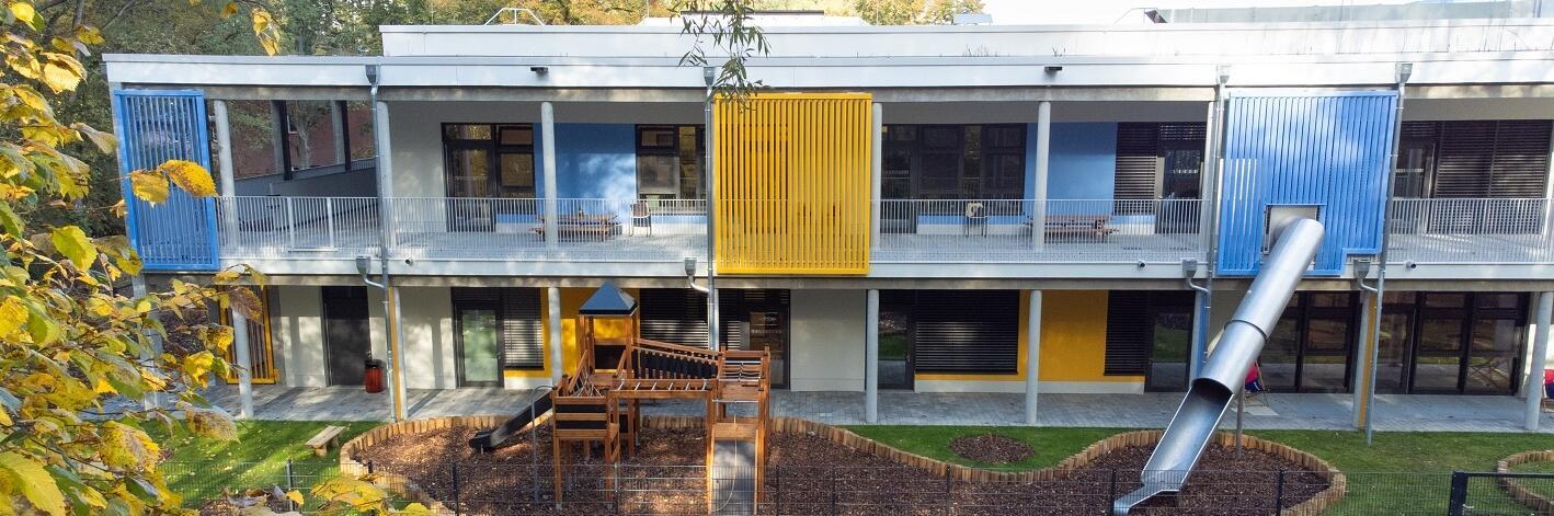 Ein Panorama der Außenansicht der Kita Lumi Natura mit Rutsche, Klettergerüst und weiterem Spielgerät.