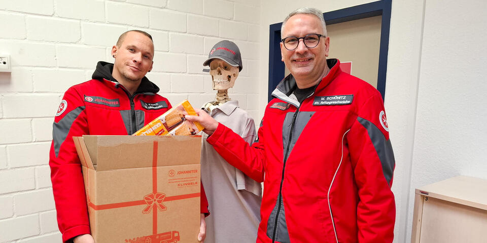 Zwei Männer mit einem offenen Paket. Einer steckt eine Kekspackung in das Paket