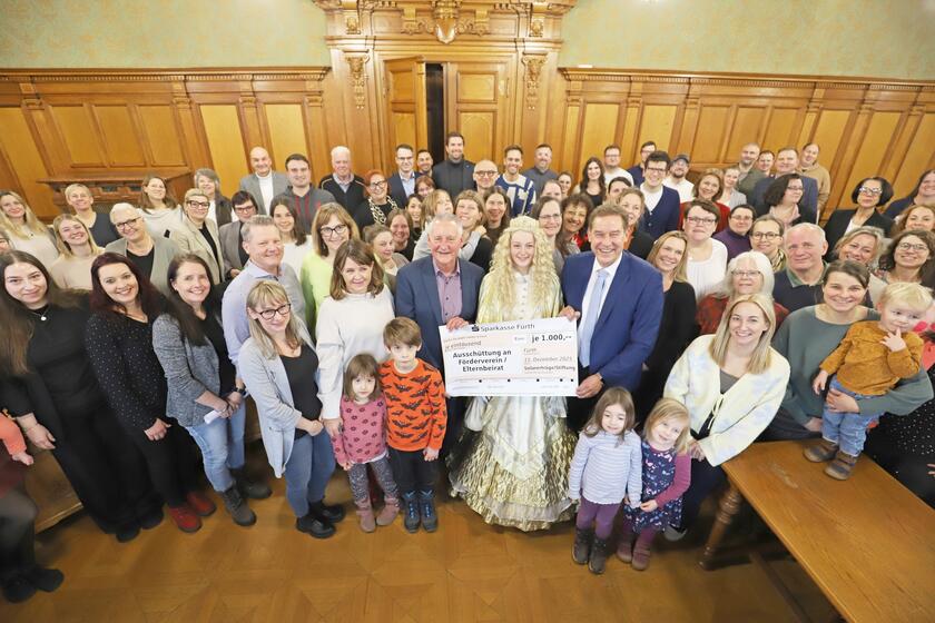 Auf einem Gruppenbild sind vielen Personen und das Christkind bei der Scheckübergabe der Stadt Fürth.
