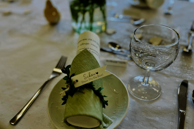 ein festliches Gedeck mit Serviette, daran ein Zettel "Schön, dass Du da bist" und einem Weinglas