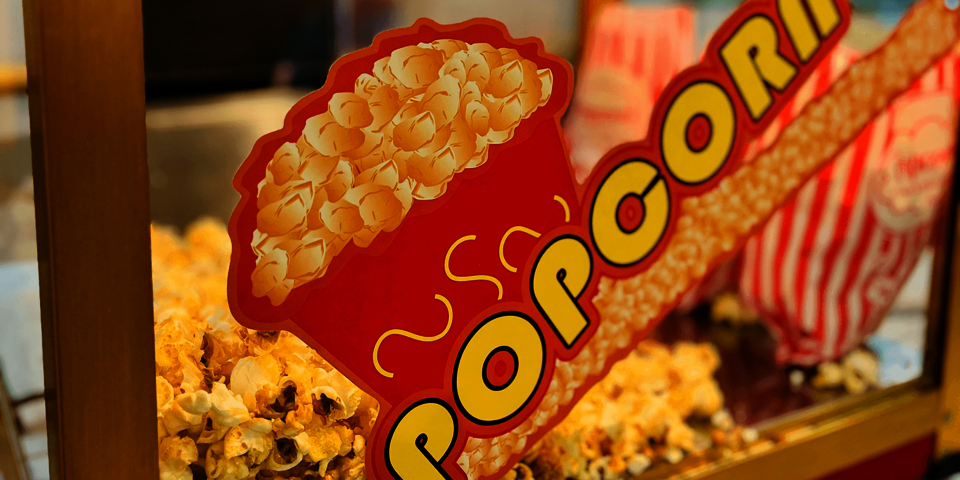 Nahaufnahme einer Popcornmaschine mit jeder Menge frischem, gelbem Popcorn und einem auffälligen roten Schild mit der Aufschrift „Popcorn“.