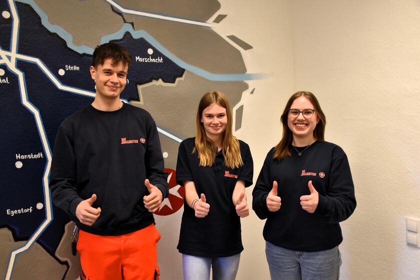 drei Freiwilligendienstleistende stehen vor der Landkarte des Landkreises Harburg und strecken den Daumen nach oben