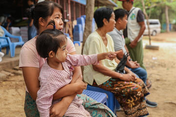Drei Kinder und zwei Erwachsene sitzen auf dem Boden in Myanmar.
