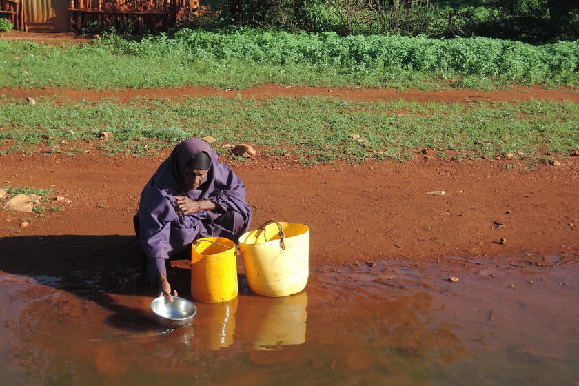 Eine ältere Dame schöpft Wasser aus dem Fluss, dessen Wasser braun ist