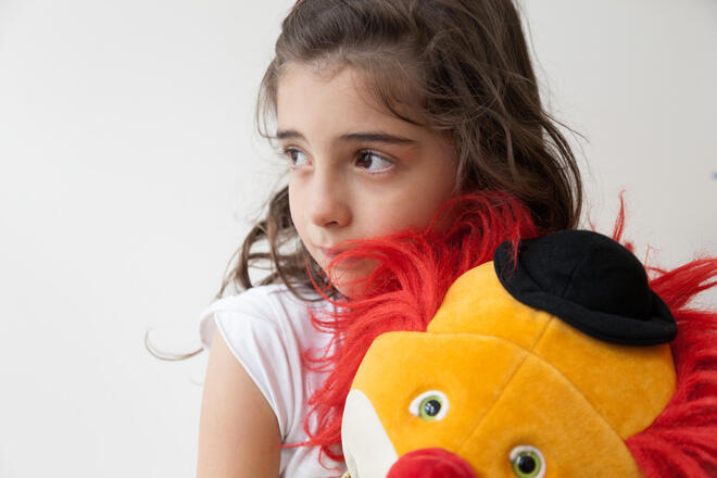 Ein Kind blickt in die Ferne und hält einen Handpuppe im Arm.