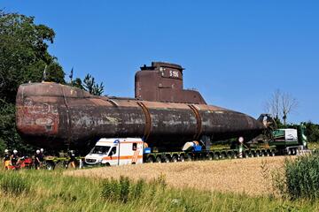 Ein Rettungswagen der Johanniter begleitet den Transport eines U-Bootes in Heilbronn. Das U-Boot wird auf einem Schwerlasttransporter über eine Straße befördert und der Rettungswagen sichert mit eingeschaltetem Blaulicht die nahe Umgebung ab