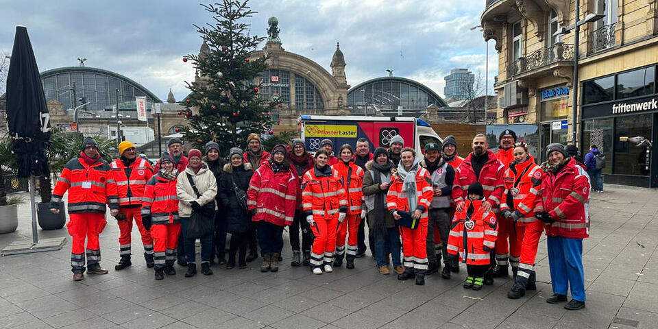 Gruppenbild aller ehrenamtlichen Helfenden mit dem Frankfurter Hauptbahnhof im Hintergrund.