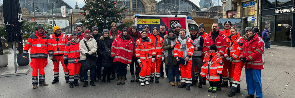 Gruppenbild aller ehrenamtlichen Helfenden mit dem Frankfurter Hauptbahnhof im Hintergrund.
