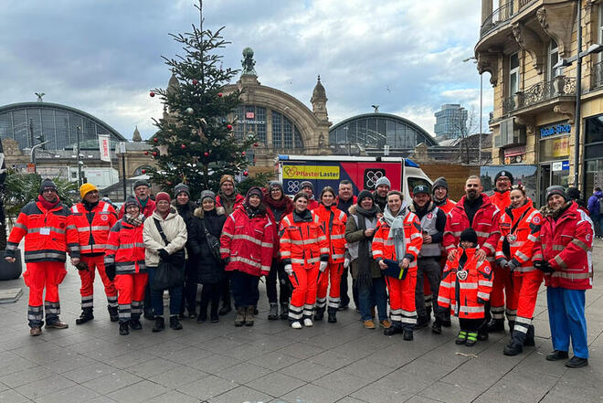 Gruppenbild aller ehrenamtlichen Helfenden mit dem Frankfurter Hauptbahnhof im Hintergrund.