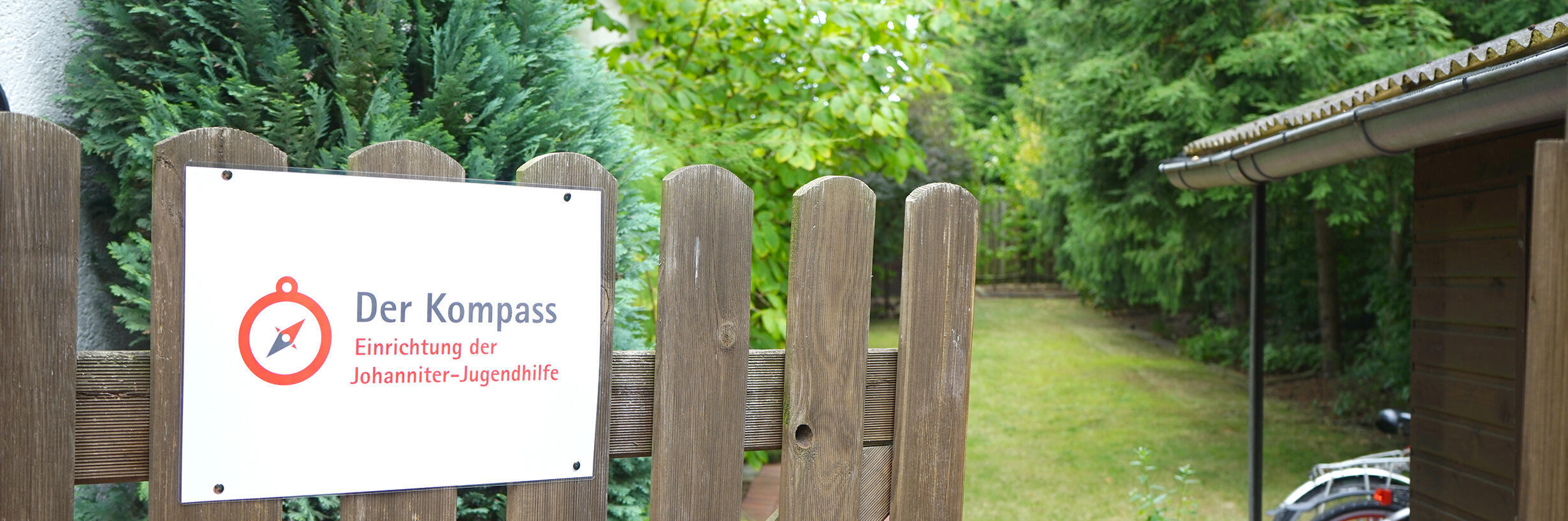 geöffnetes Gartentor mit Schild "Johanniter-Jugendhilfe Kompass"