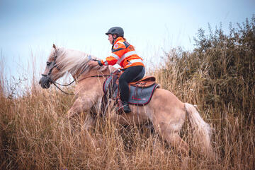 Eine Johanniter-Einsatzkraft reitet auf einem Pferd.