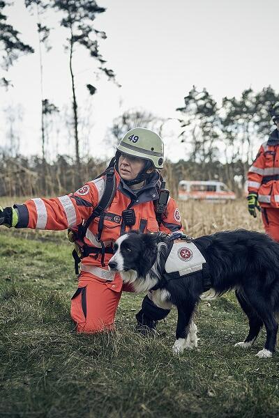 Zwei Einsatzkräfte der Rettungshundestaffel mit einem Rettungshund im Wald