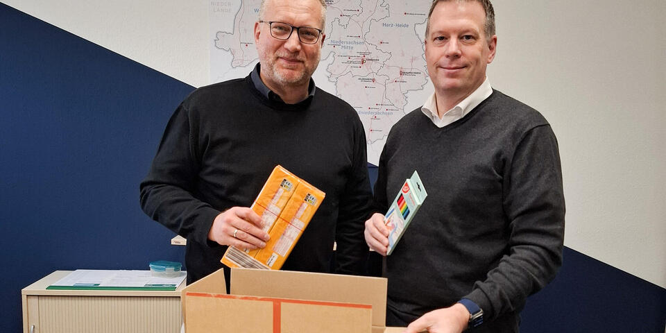 Zwei Männer mit einem offenen Paket. Sie halten Kekse und Bundstiftpackungen in den Händen