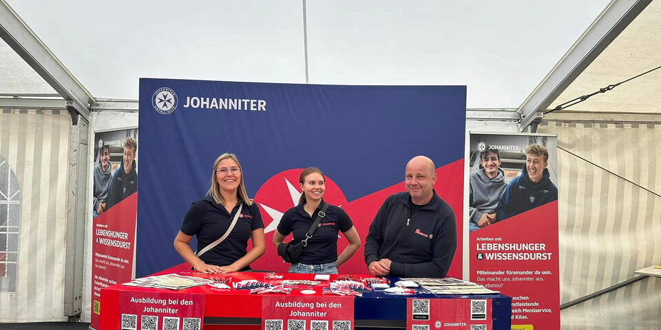 Zwei Johanniterinnen und ein Johanniter vor einem Messestand