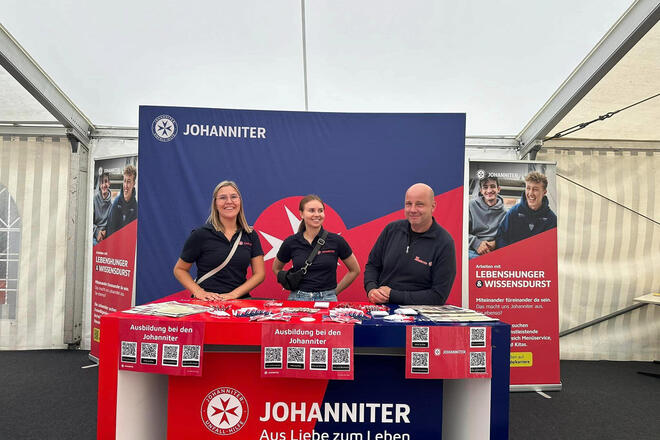 Zwei Johanniterinnen und ein Johanniter vor einem Messestand