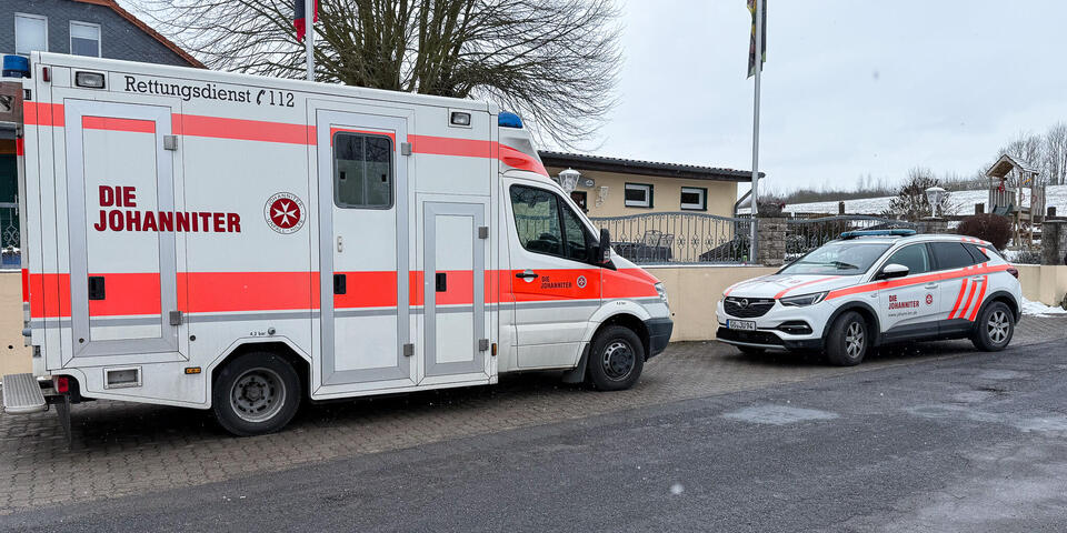 Ein Johanniter-RTW und ein Johanniter-Auto auf einer Straße in einem Wohngebiet