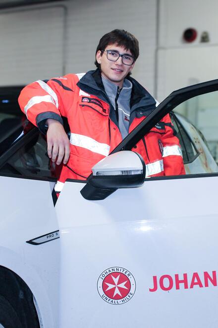 Ein junger Mann steht an einem Johanniter-Fahrzeug