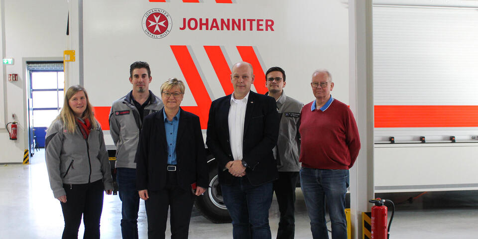 Vier Männer und zwei Frauen vor einem gerätewagen mit Johanniter-Logo.