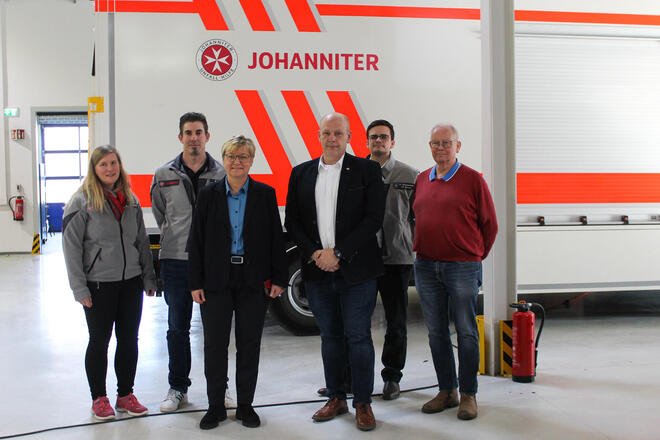 Vier Männer und zwei Frauen vor einem gerätewagen mit Johanniter-Logo.