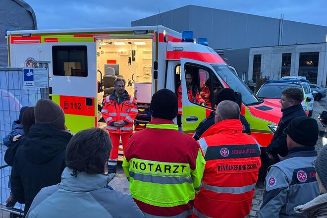 vor einem Rettungswagen der Johanniter haben sich Menschen versammelt, um ihn in den Dienst zu stellen.