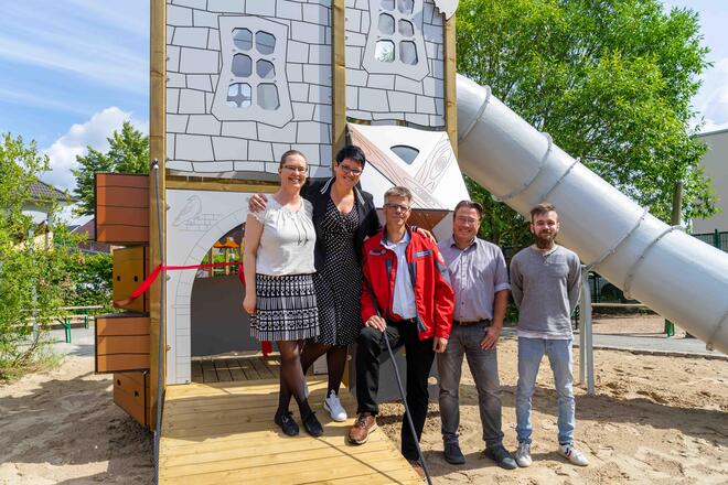 Einweihung neues Außengelände Johanniter-Kita Zwergenwache Auf dem Bild stehen fünf Personen vor der Ritterburg, einem Spielelement der Kita.