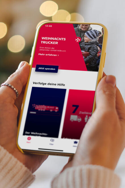 Hände halten ein Smartphone in der Hand, auf dem Informationen zum Johanniter-Weihnachtstrucker zu sehen sind