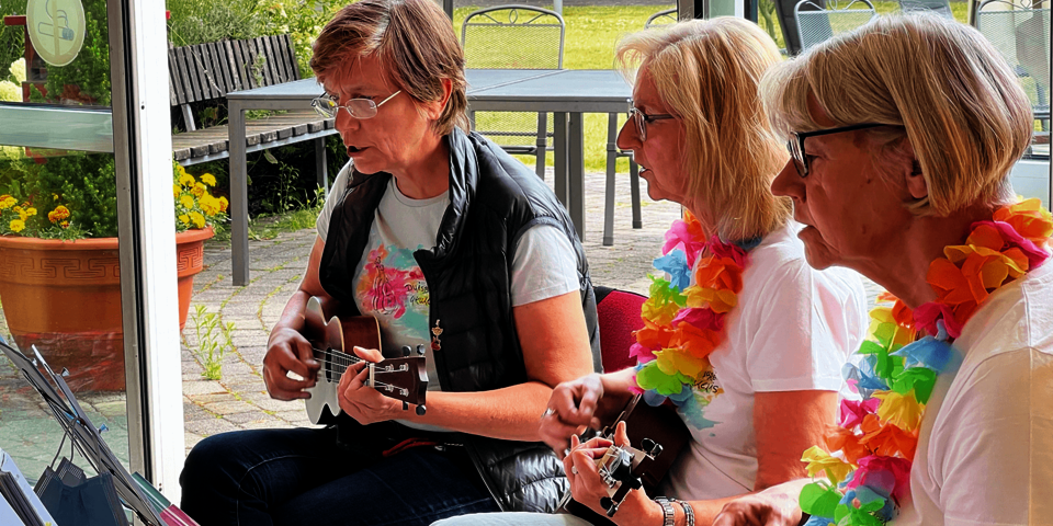 Drei Frau sitzen nebeneinander mit Instrumenten und Blumenkränzen