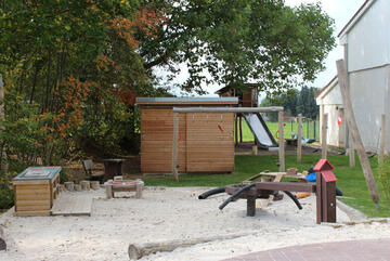 Sandkasten und weitere Holzspielgeräte und ein Holzhäuschen.