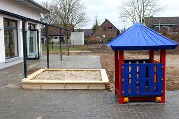 Sandkasten mit einem blau-rotem Spielhäuschen.