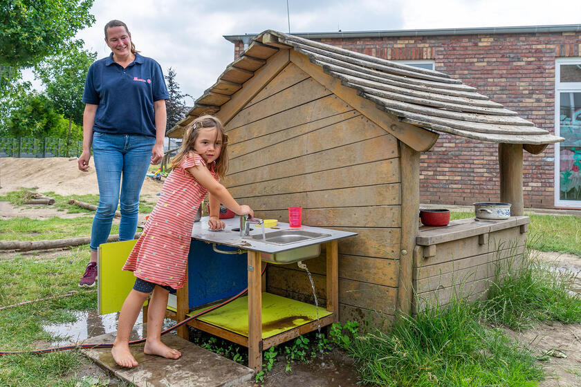 Wasser marsch: Zoe aus der Eichhörnchen-Gruppe zeigt, wie die Matschküche funktioniert, nachdem Kita-Leiterin Sarina Wünsch-van Herwaarden den Schlauch angeschlossen hat.