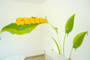 Eine gemalte Raupe mit Blättern übers Eck auf zwei Wände verteilt in grün und gelb gehalten