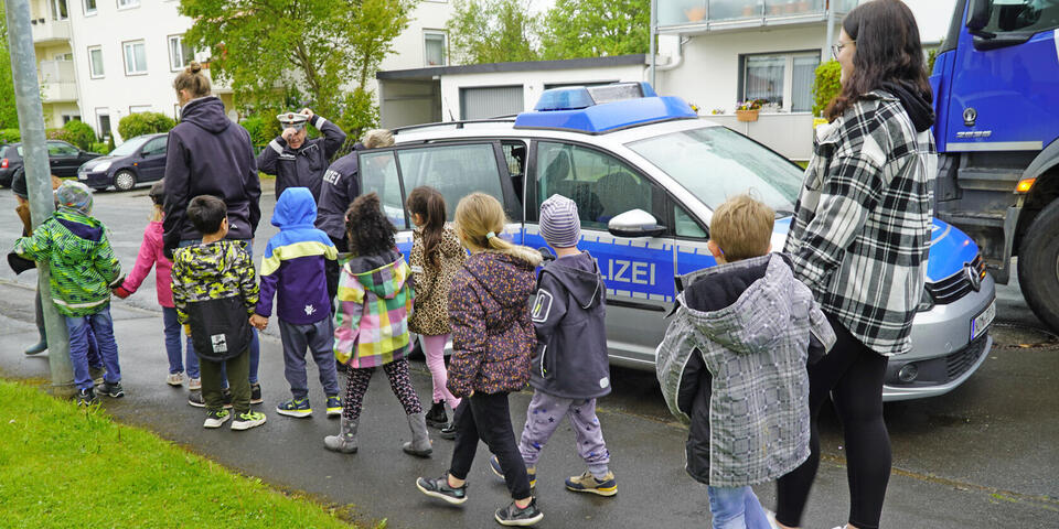 Kinder gehen neben einem Polizeiwagen auf einem Weg entlang