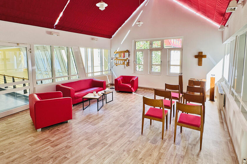 Raum der Stille in warmen Rottönen mit Lesesofa und Altarbereich