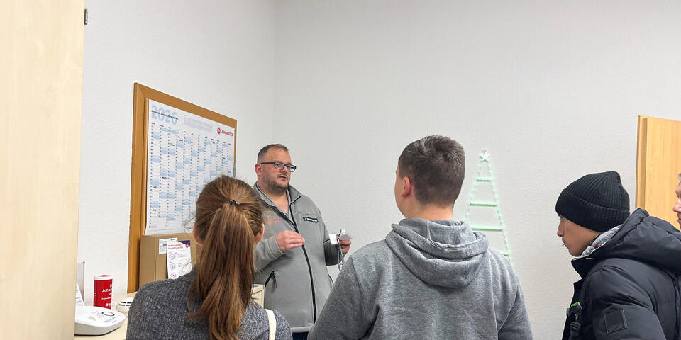 Zwei Schüler und eine Schülerin hören einem Mann in Johanniter-Bekleidung zu